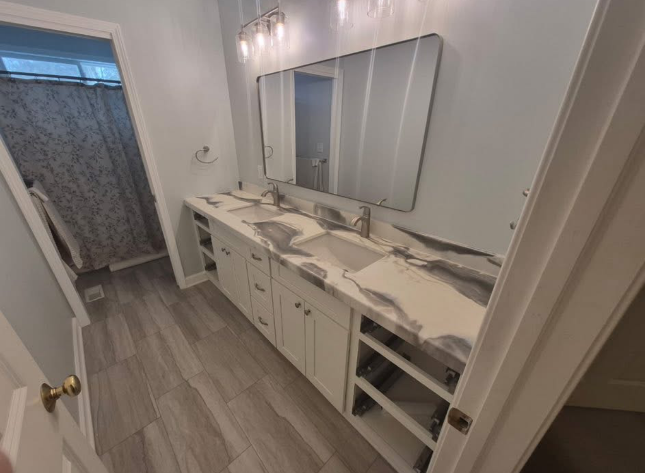 A modern bathroom vanity with a marbled countertop, white cabinets, and an open shelving unit, adjacent to a shower area.