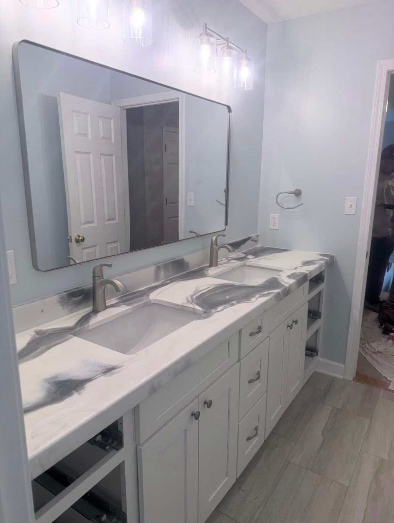 A bathroom vanity with a long mirror, white cabinets, and a white countertop with gray marbling streaks.