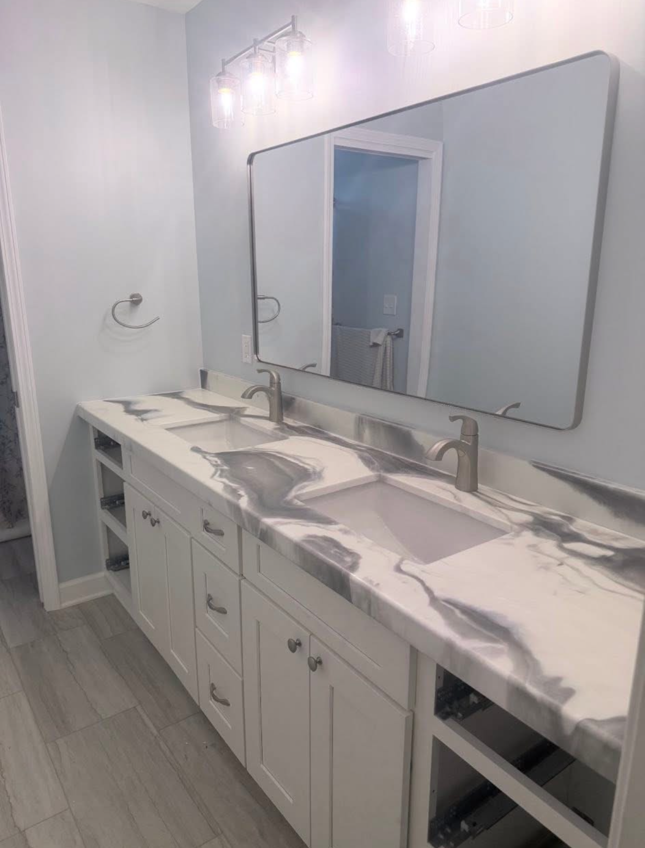 A bathroom vanity with white cabinets, double sinks, and a large, rectangular mirror on a light blue wall.