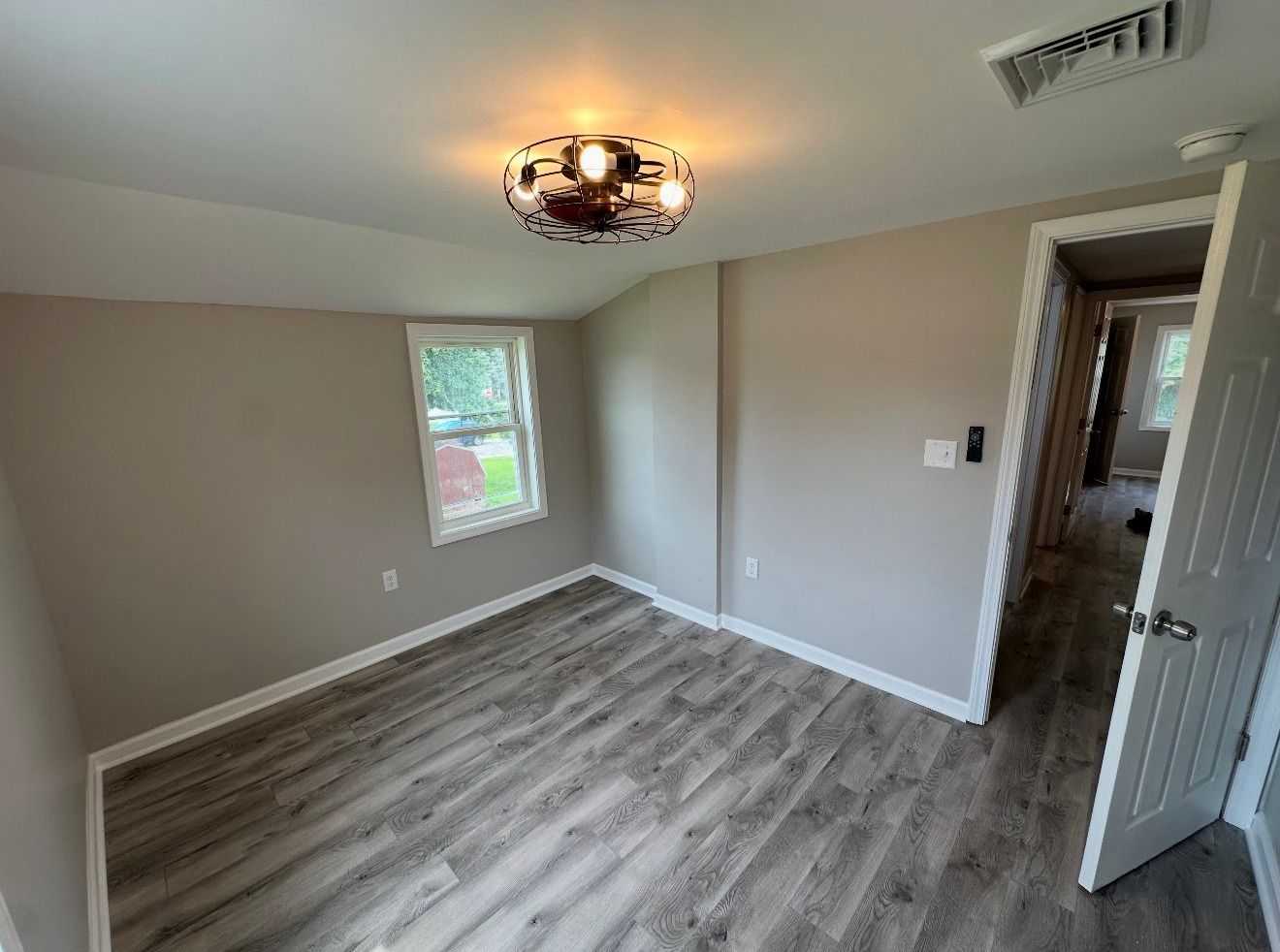 Empty room with light gray walls, wood-look floor, window, and open door.
