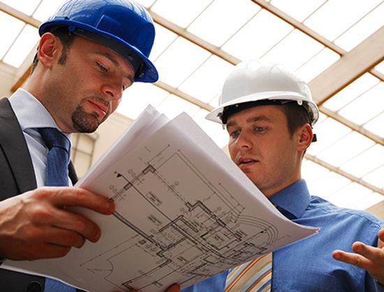 Two men wearing hard hats are looking at a blueprint