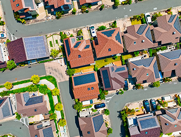 An aerial view of a residential area with lots of houses and solar panels on the roofs.