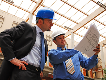 Two men wearing hard hats are looking at a blueprint