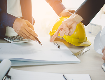 A group of people are sitting at a table looking at papers and a hard hat.