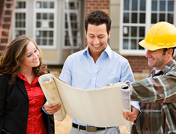 A man and a woman are standing next to a construction worker looking at a blueprint.