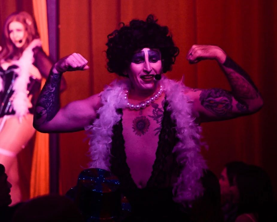 A man is flexing his muscles while wearing a feather boa — Lux Noir In  Townsville City, QLD