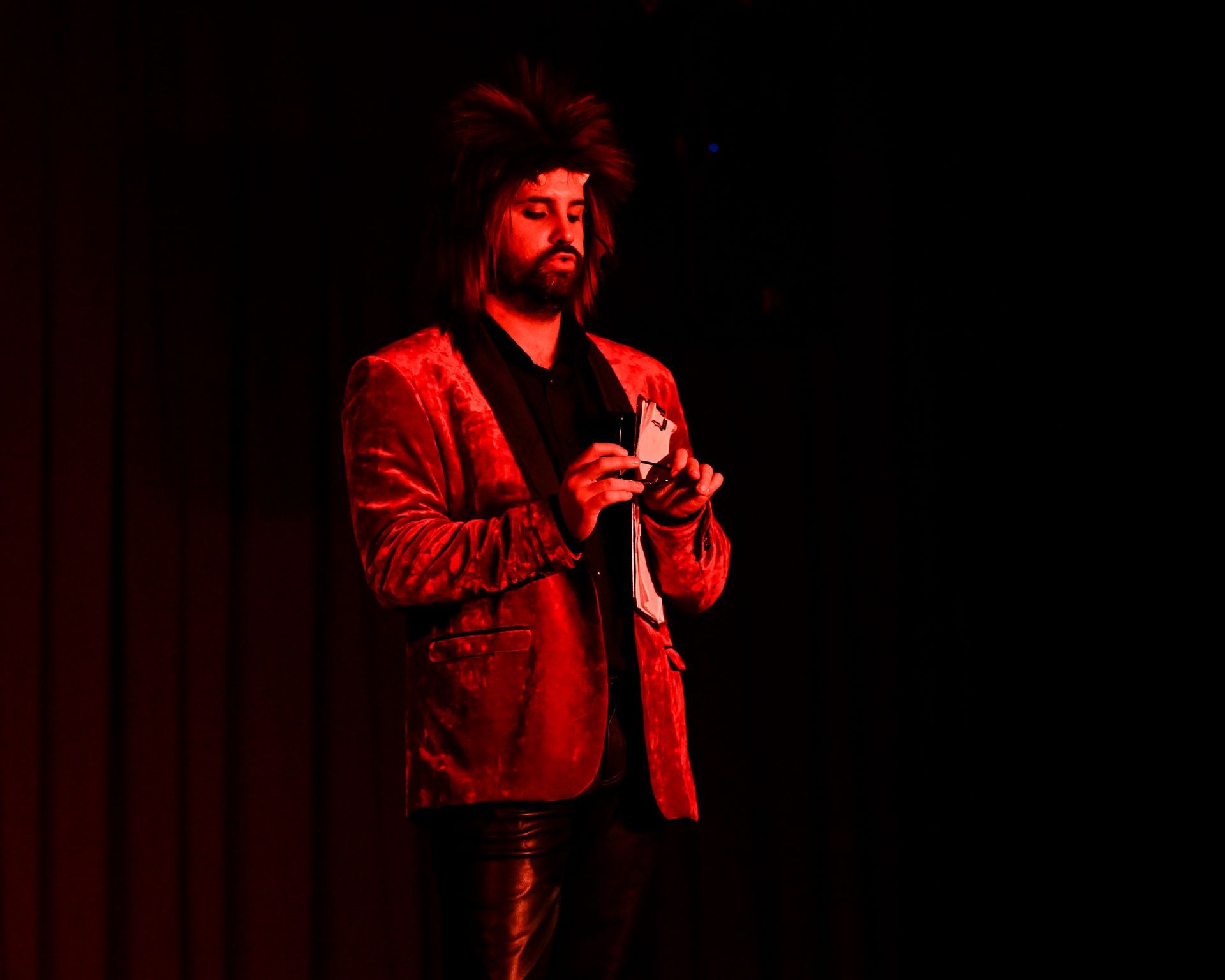 A man in a red jacket is standing in front of a red curtain holding a card — Lux Noir in Townsville City, QLD