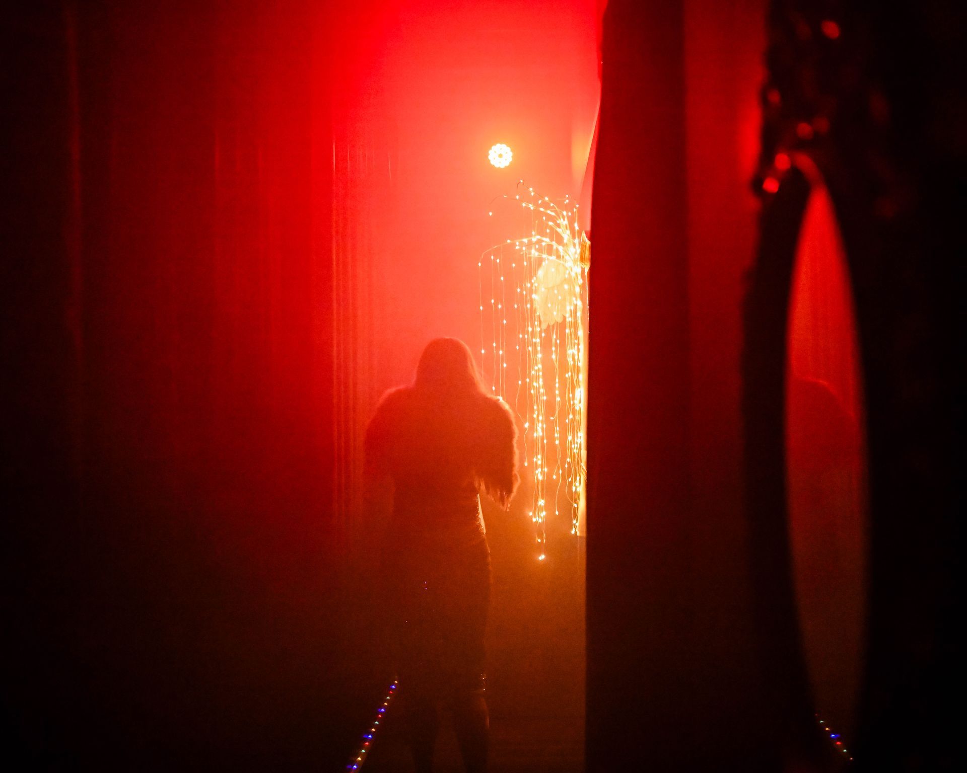 A person is standing in a dark room with a red light behind them— Lux Noir in Townsville City, QLD