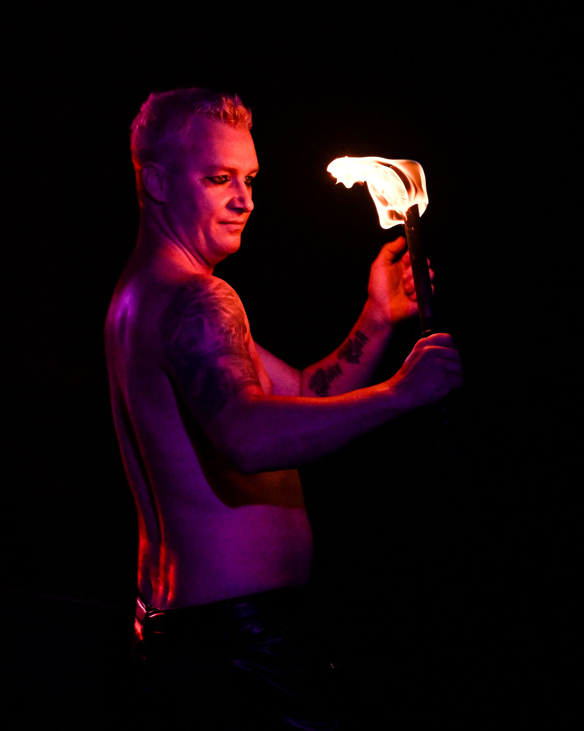 A shirtless man is holding a fire torch in a dark room— Lux Noir in Townsville City, QLD