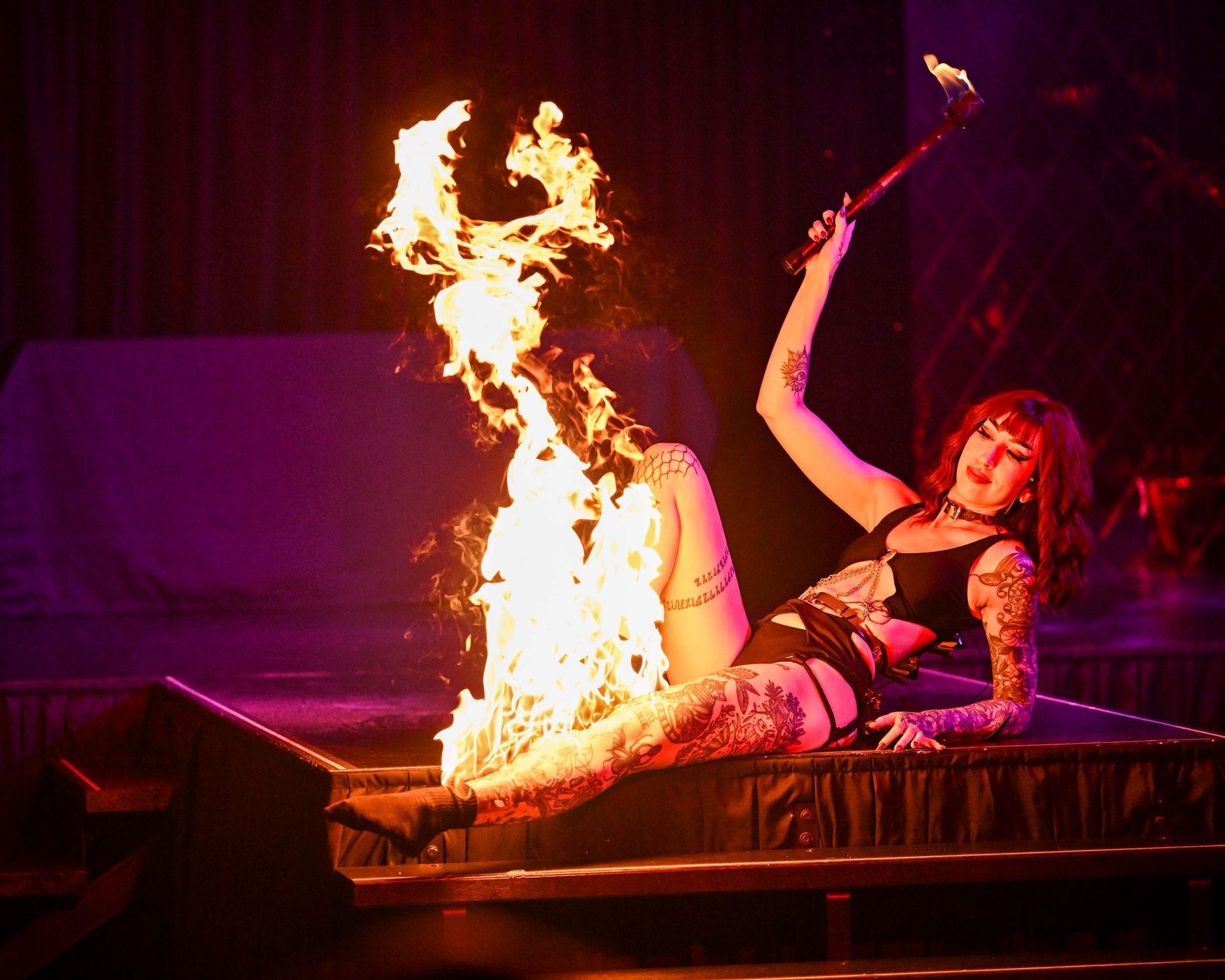 A woman is laying on her stomach on a stage with flames coming out of her feet— Lux Noir in Townsville City, QLD
