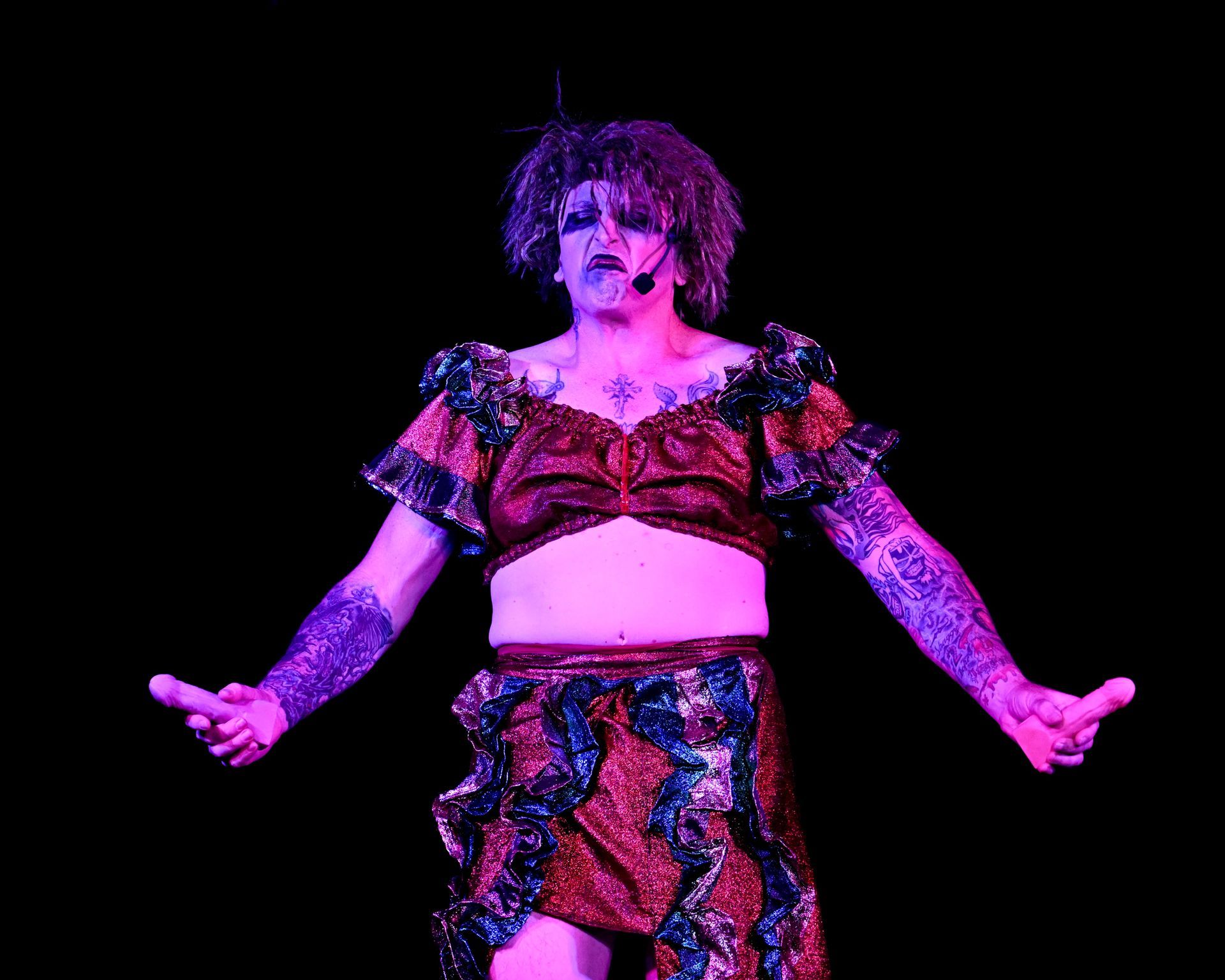 A man in a crop top and skirt is standing on a stage with his arms outstretched — Lux Noir in Townsville City, QLD