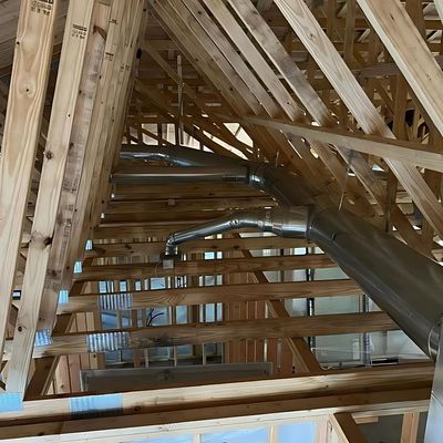 The inside of a building under construction with wooden beams and metal pipes.