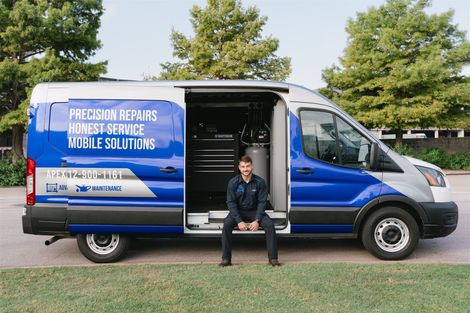 Man in uniform sits in open van door; blue and silver vehicle with company logo. | Apex Mobile Autoworks