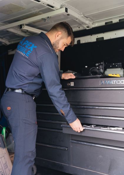 Man in blue uniform opens toolbox drawer in a van, presumably for repairs. | Apex Mobile Autoworks