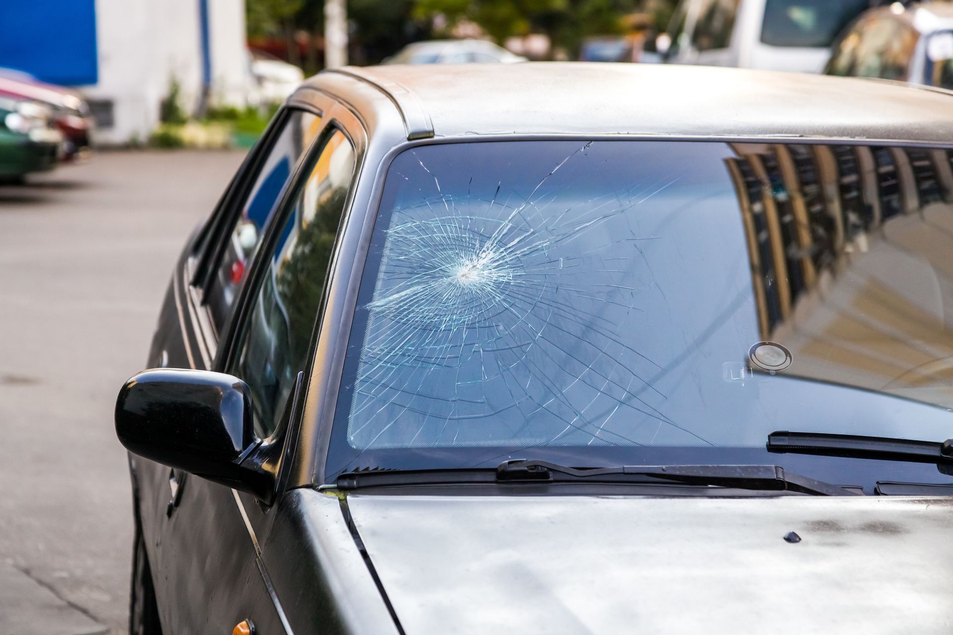A car with a broken windshield is parked in a parking lot.