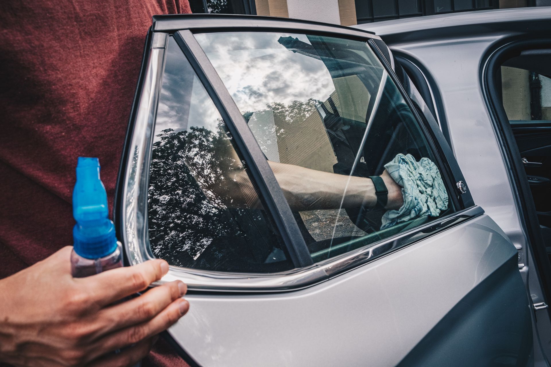 A man is cleaning a car window with a spray bottle.