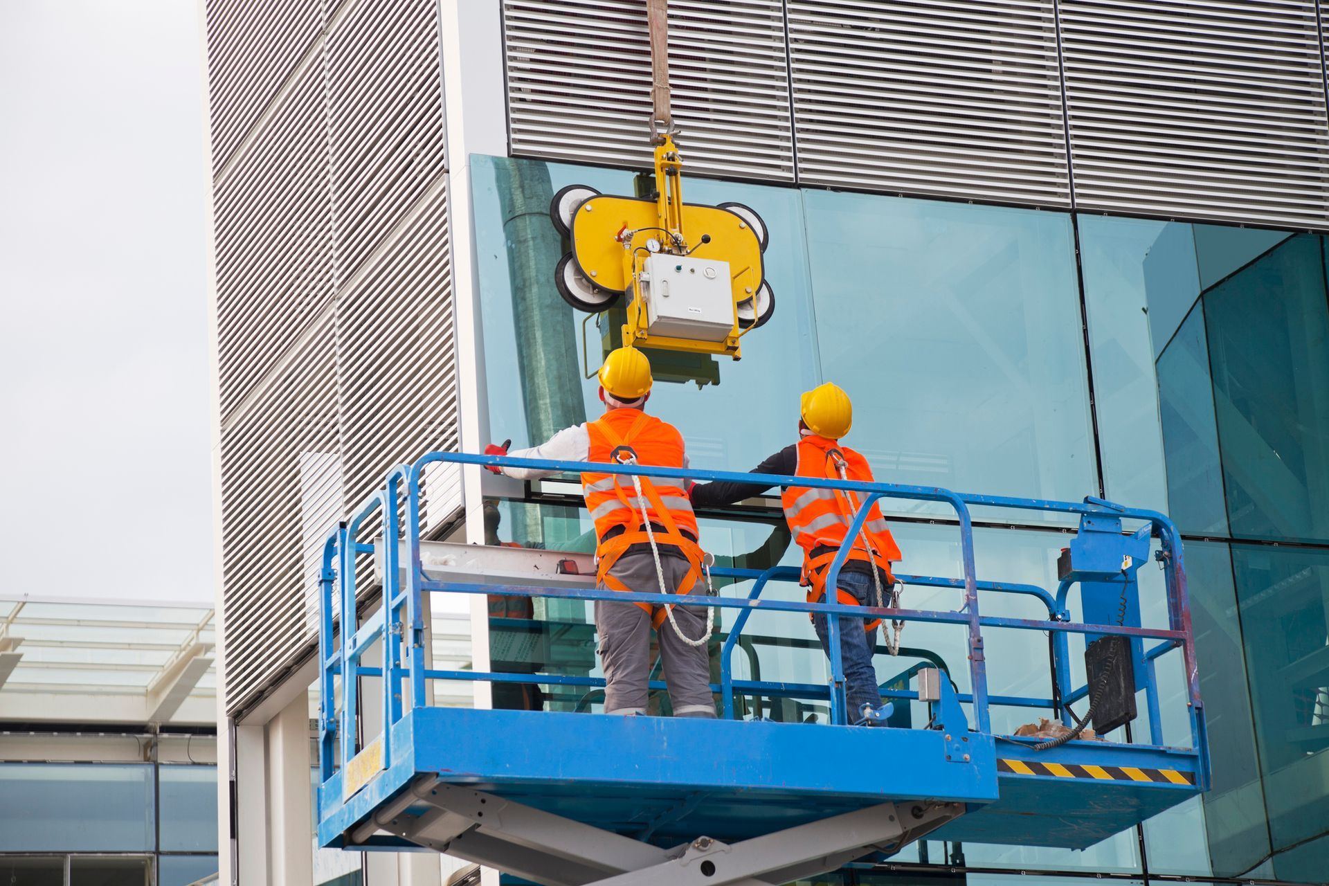 Two construction workers are installing a glass facade on a building.