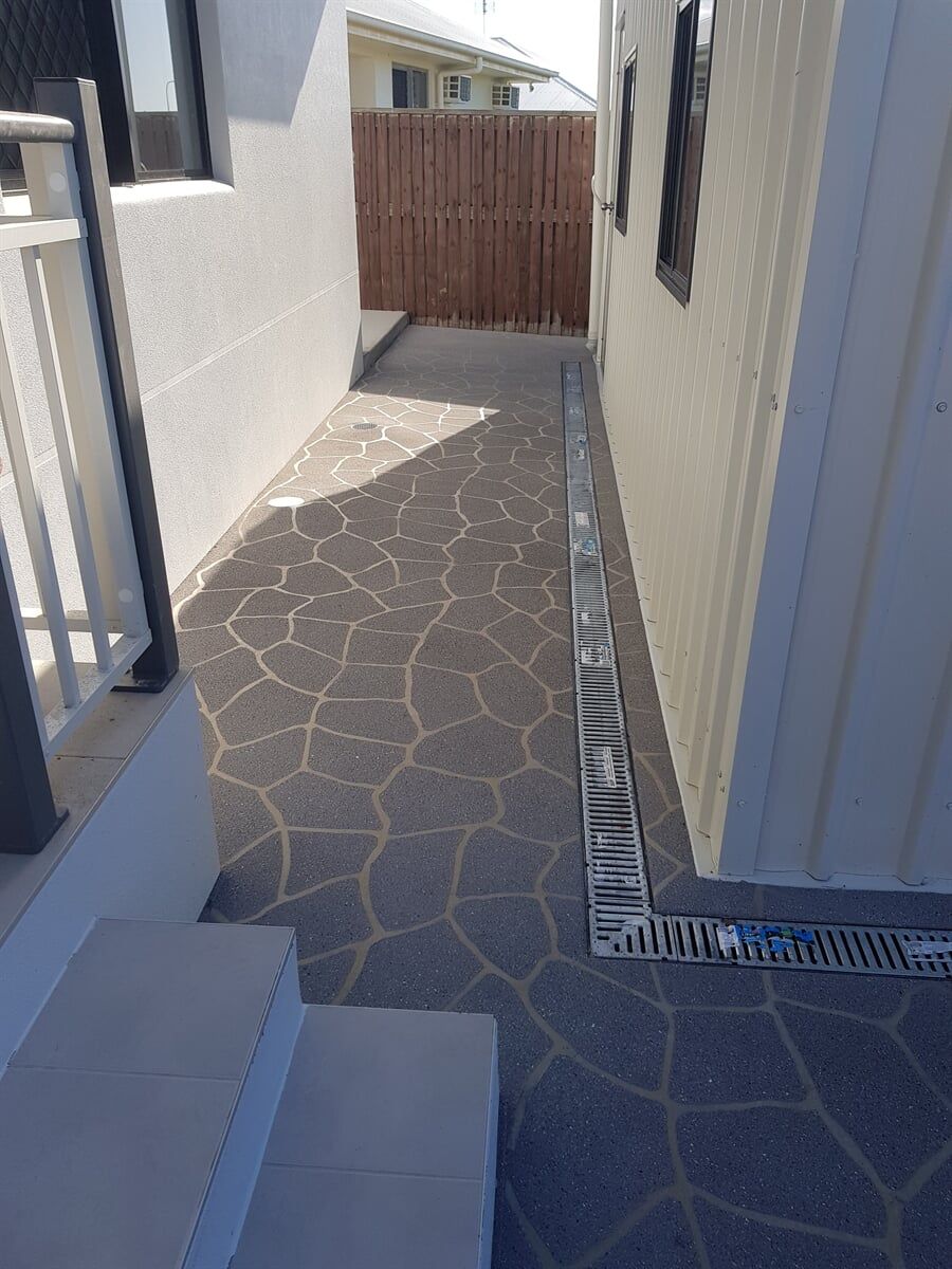 A narrow walkway between two buildings with a wooden fence in the background. — Diamond Concreting In Mount Low, QLD