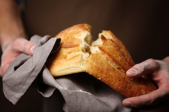 una persona spezzando in due un pezzo di pane