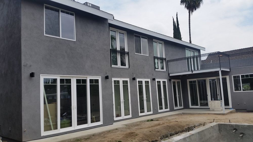 Two-story home with dark gray stucco exterior, white-framed windows, and a backyard.