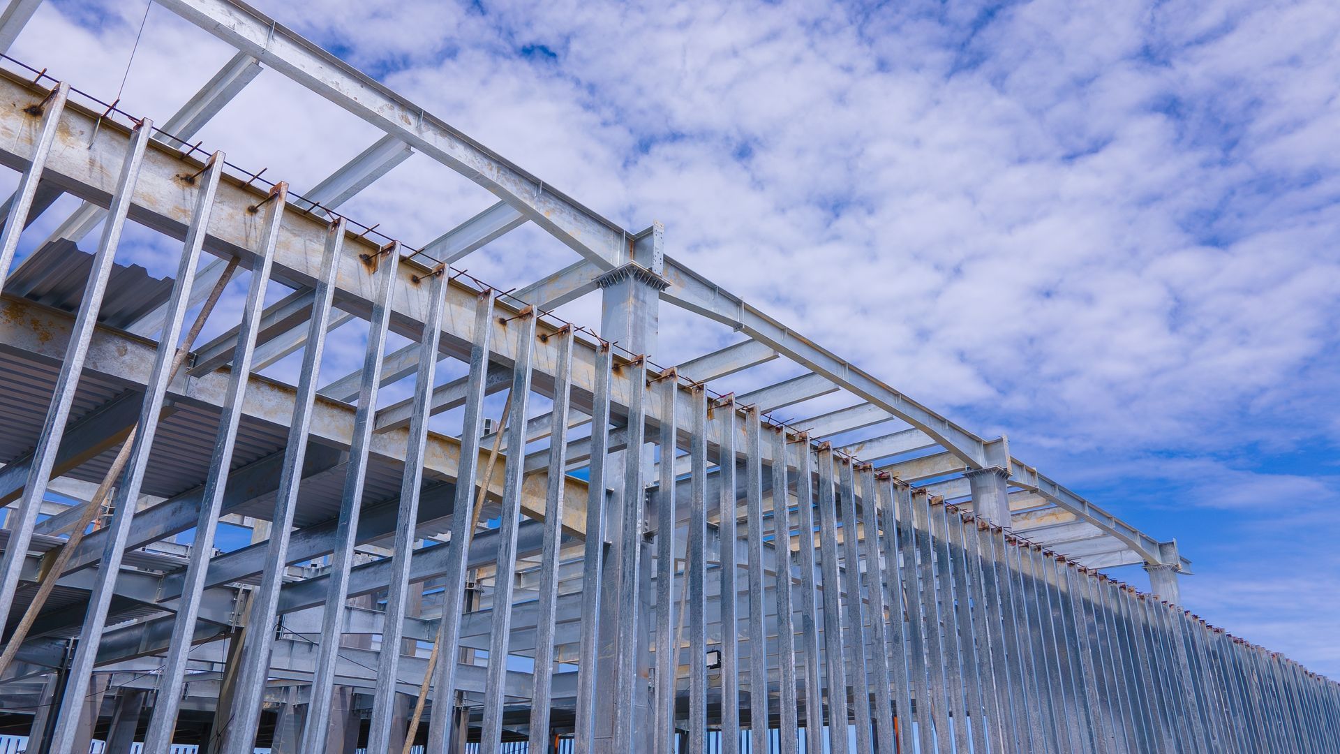 Steel framework of a building under construction against a cloudy blue sky.