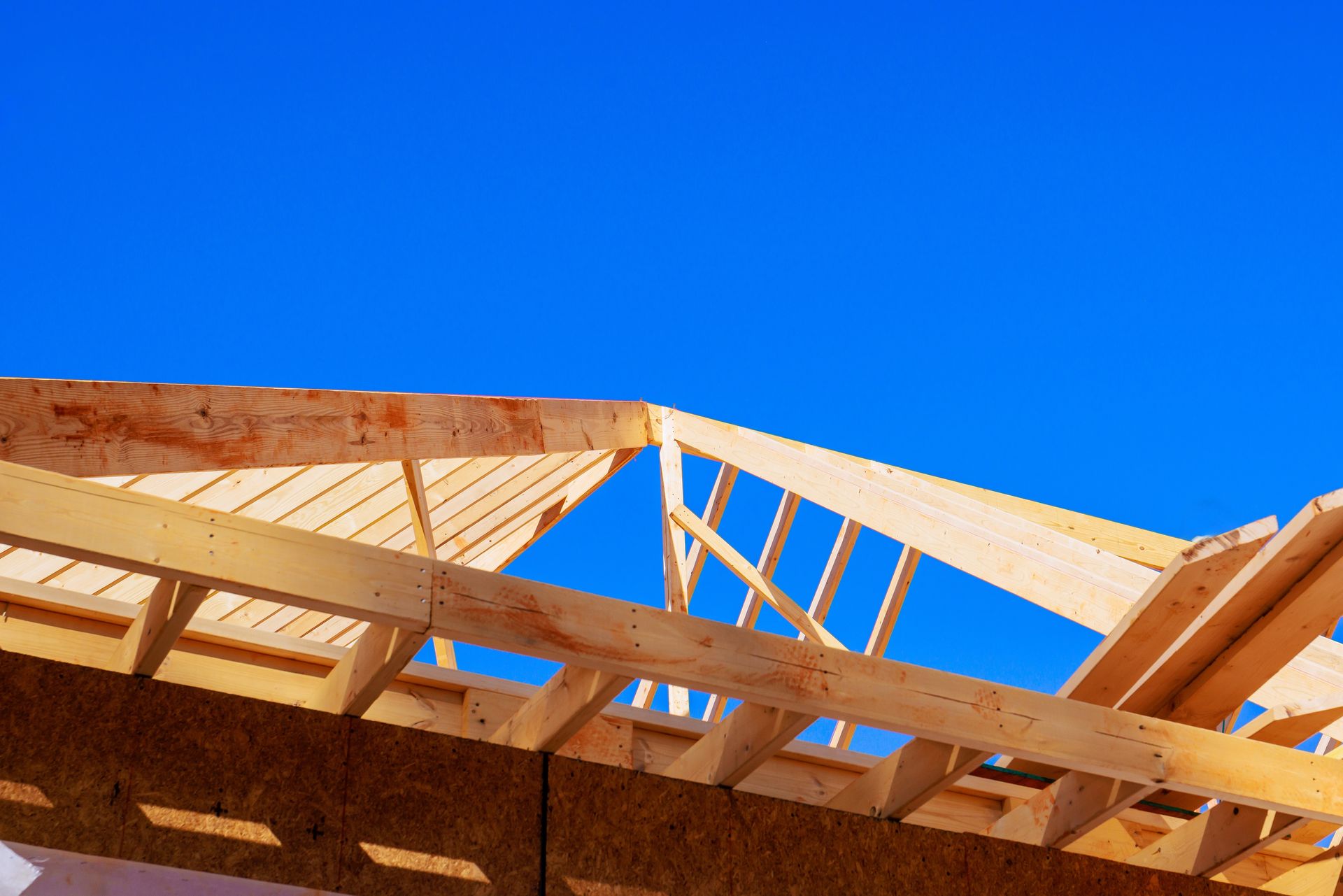 Wooden roof trusses against a bright blue sky.