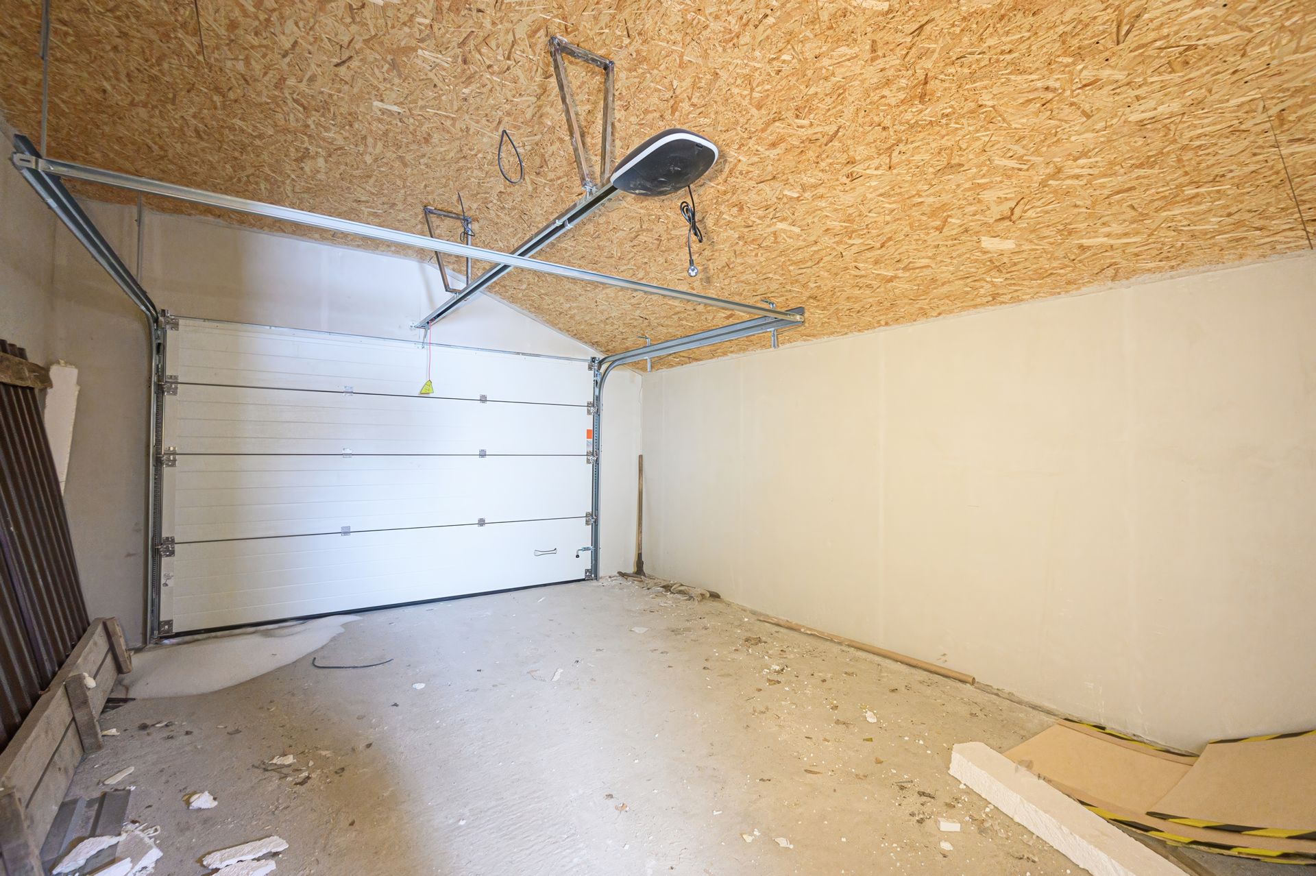 Empty garage with a closed white door and exposed ceiling.
