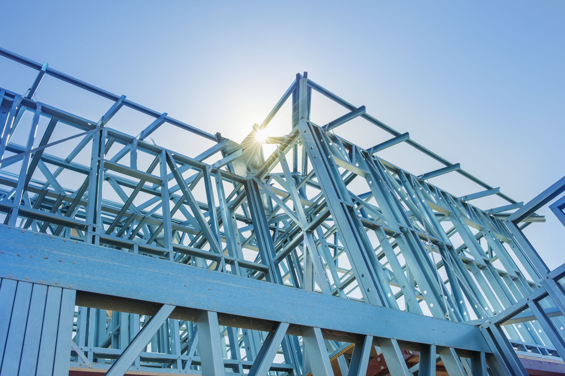 Blue steel frame of a building under construction, against a bright, sunny sky.