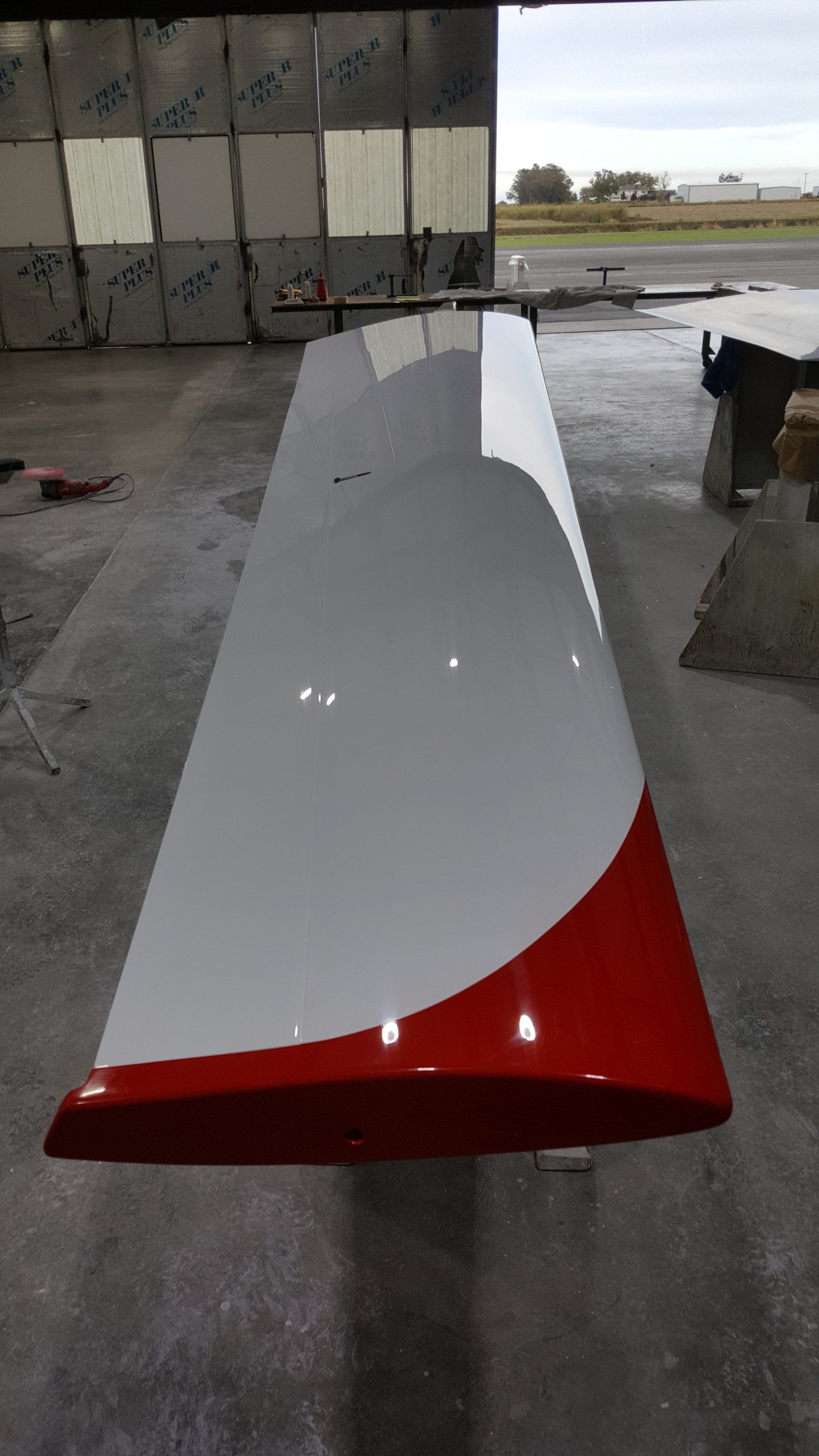 A red and white plane wing is sitting in a garage.