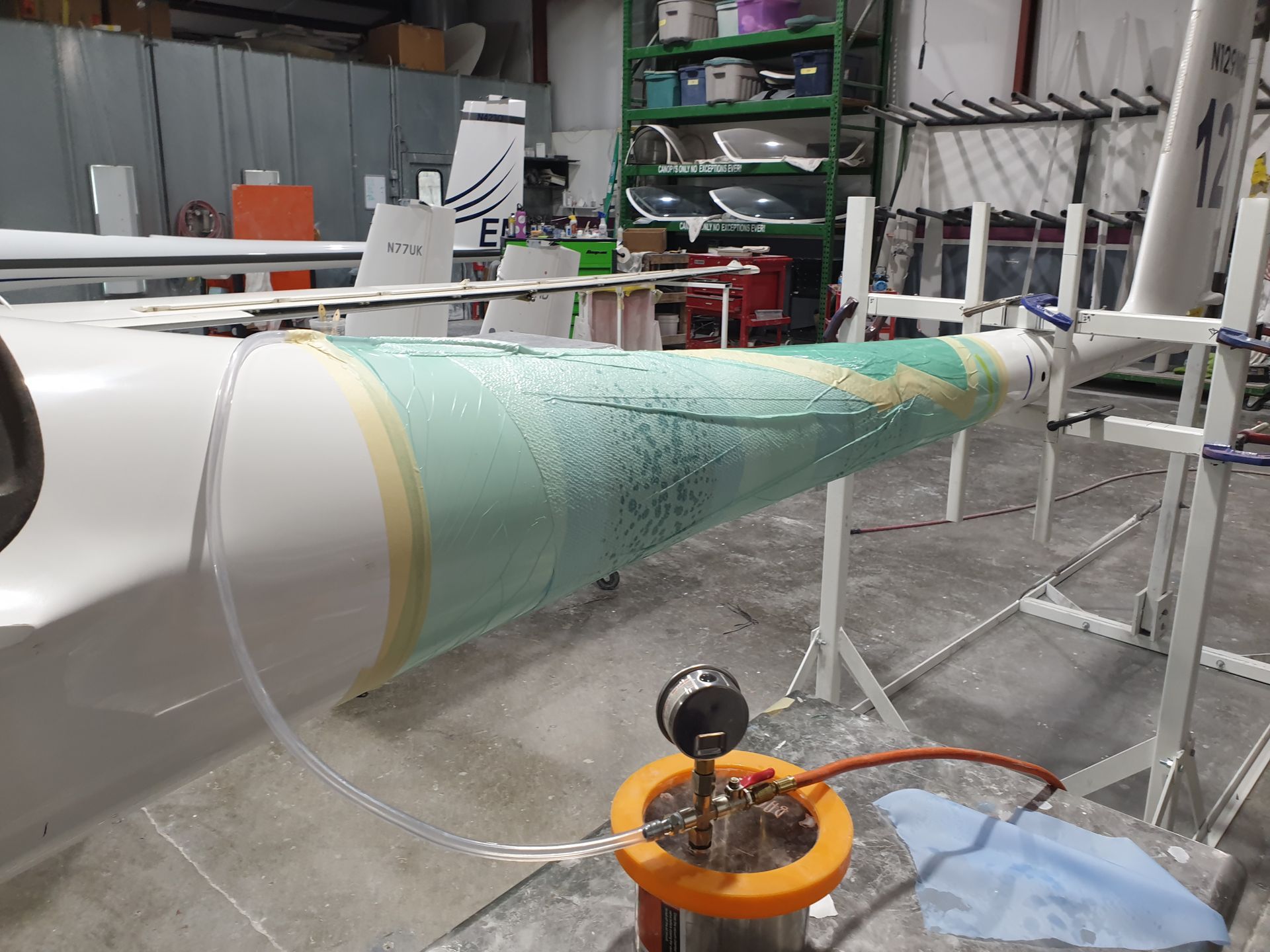 A plane is being painted in a factory with a hose attached to it.
