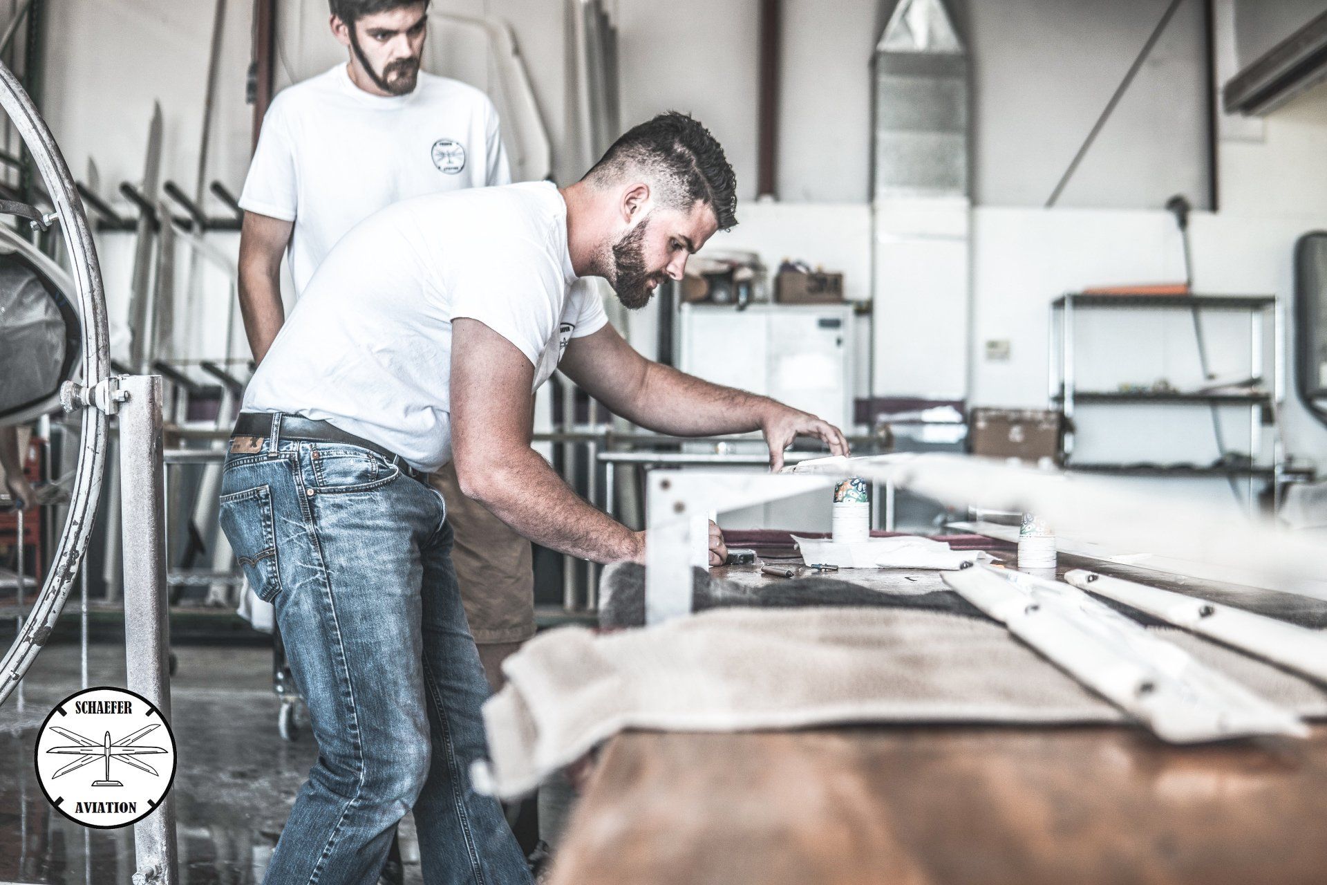 Two men are working on a piece of wood in a workshop.