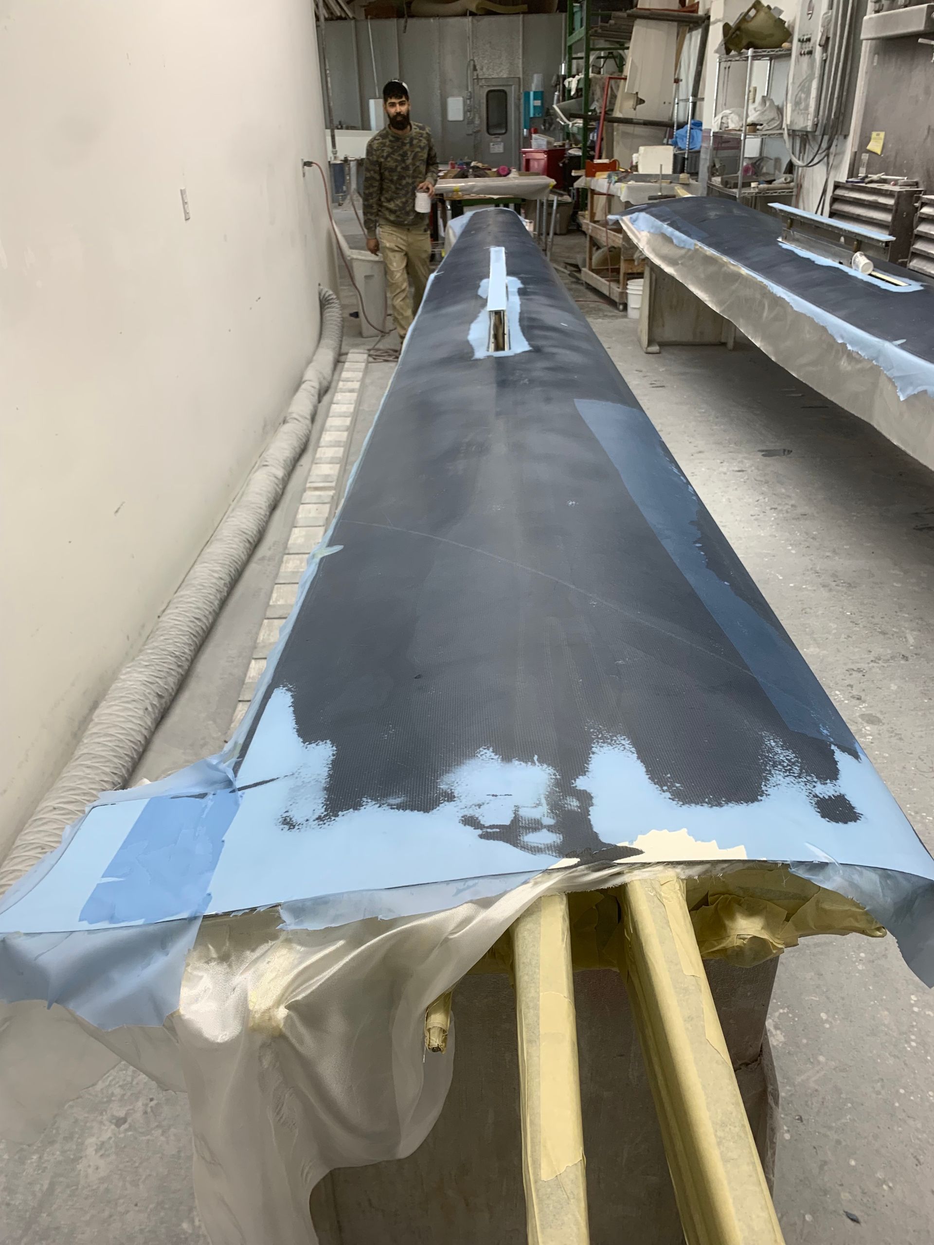 A man is standing next to a long piece of metal that is being painted.