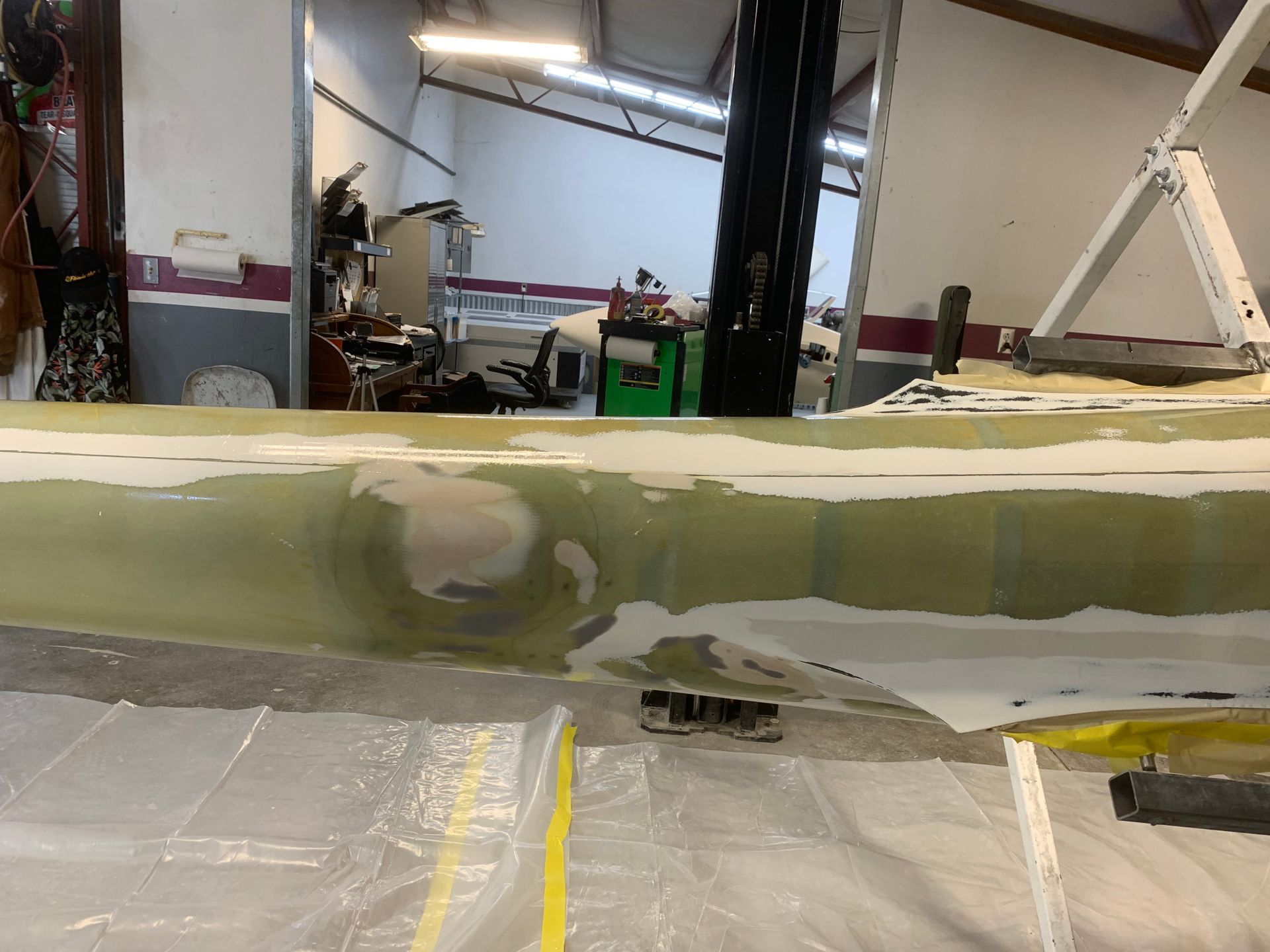 A boat is being repaired in a garage with a forklift in the background
