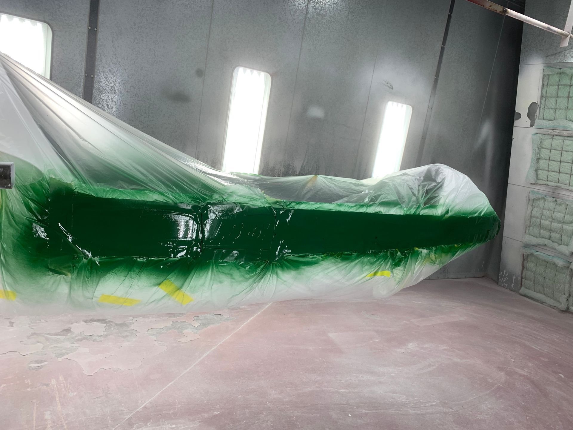 A green car is being painted in a paint booth.