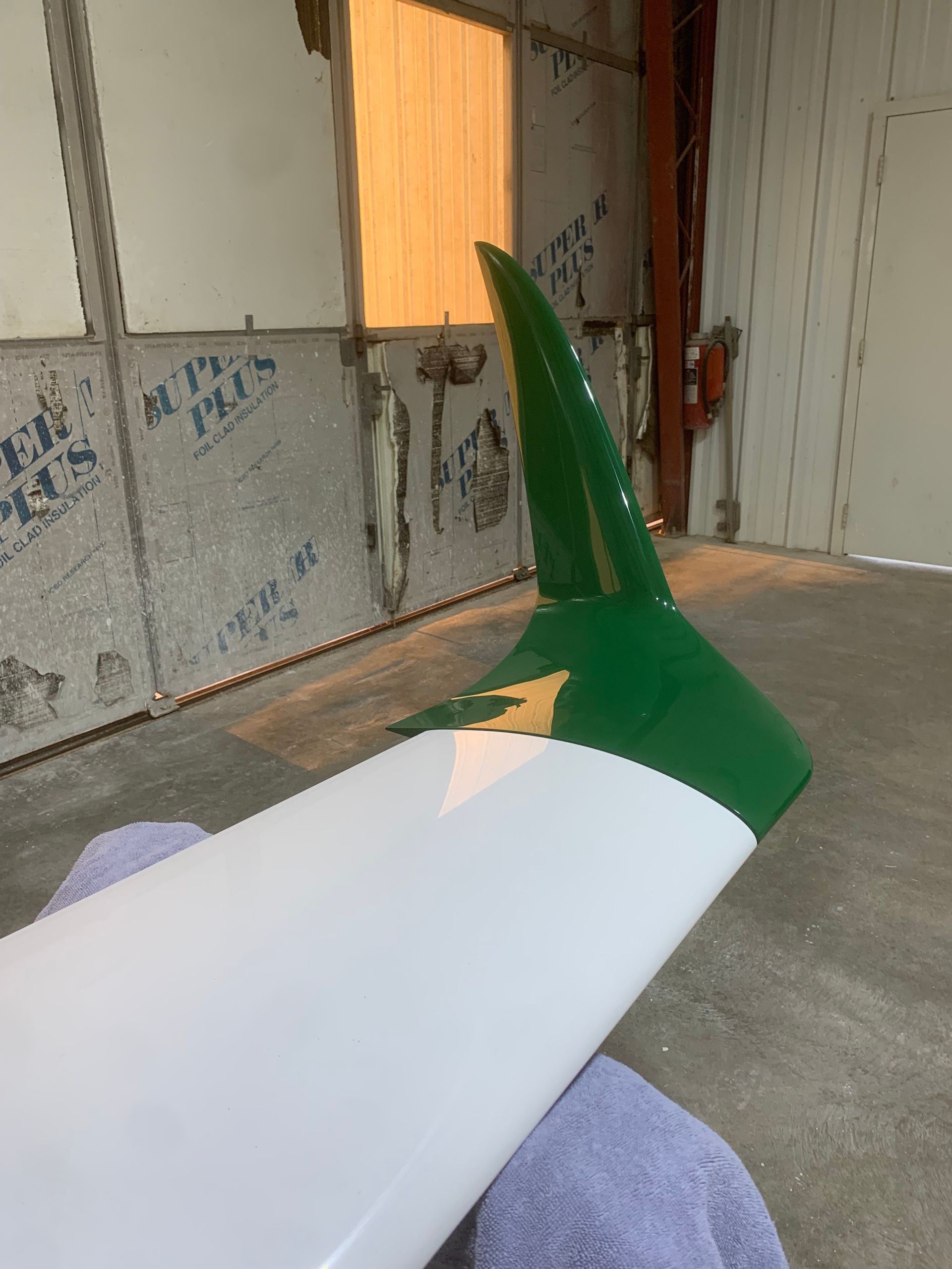 A green and white surfboard is sitting on a towel in a room.