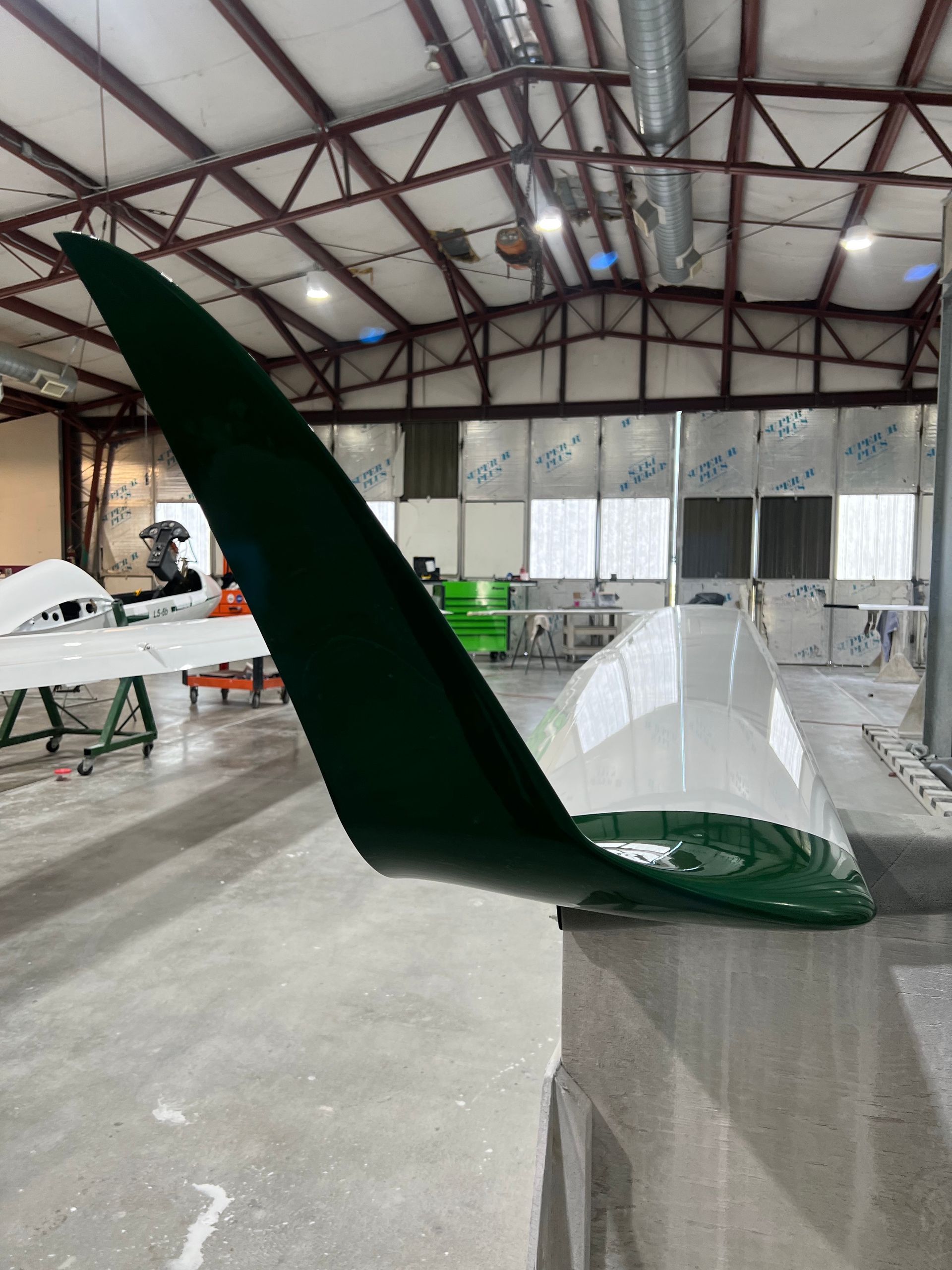A green wing of an airplane is sitting in a warehouse.