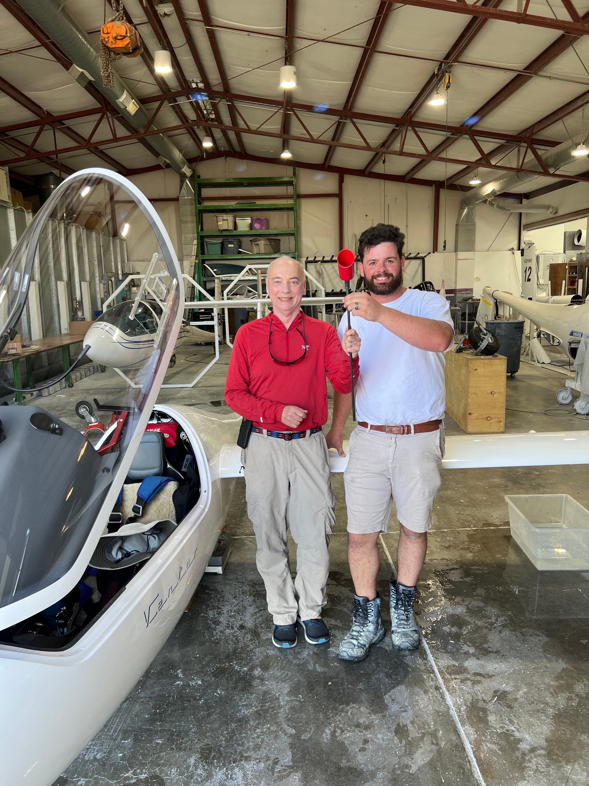 Two men are standing in front of a plane in a hangar.