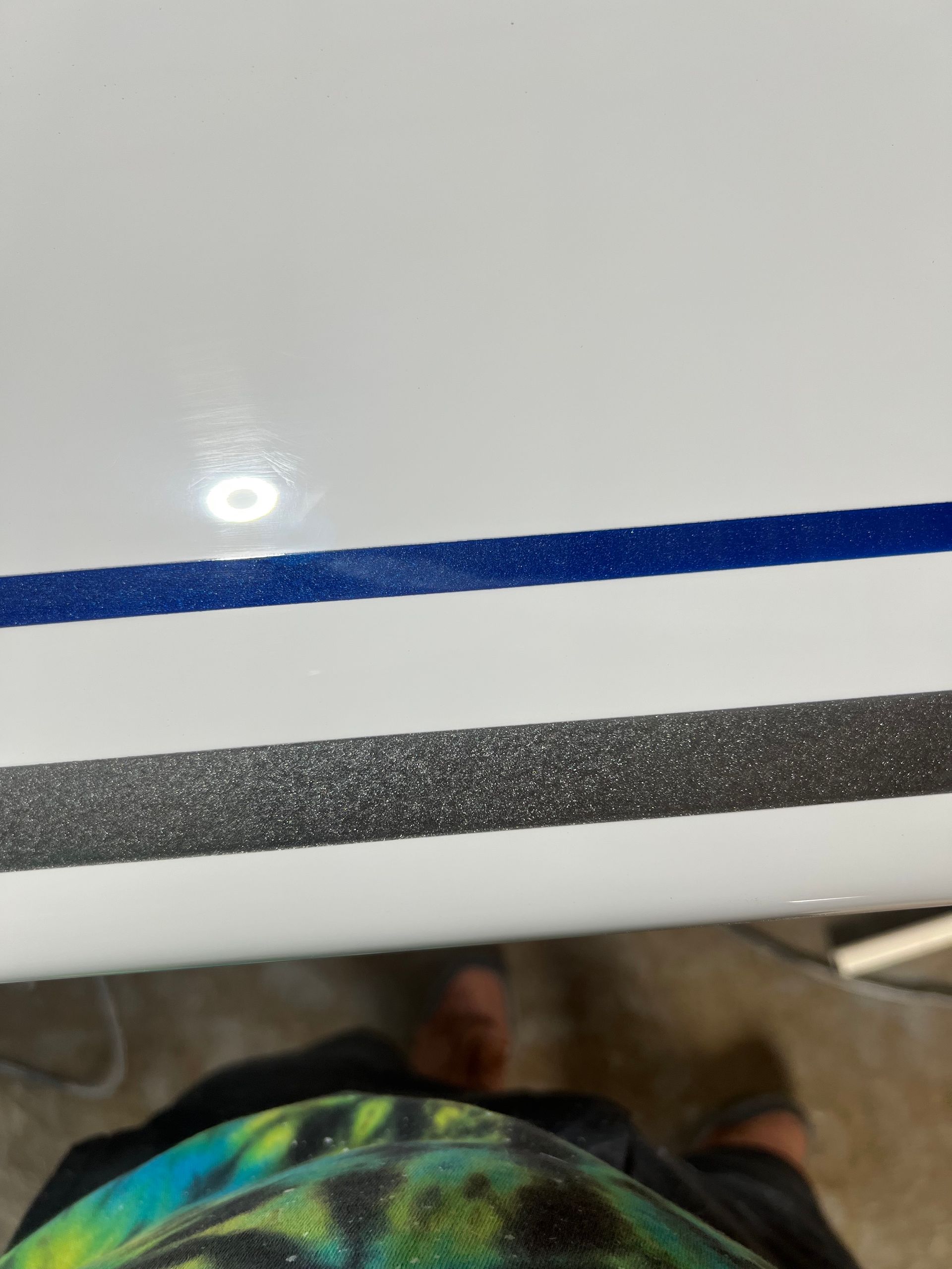 A person is standing next to a white surface with a blue and gray stripe on it.