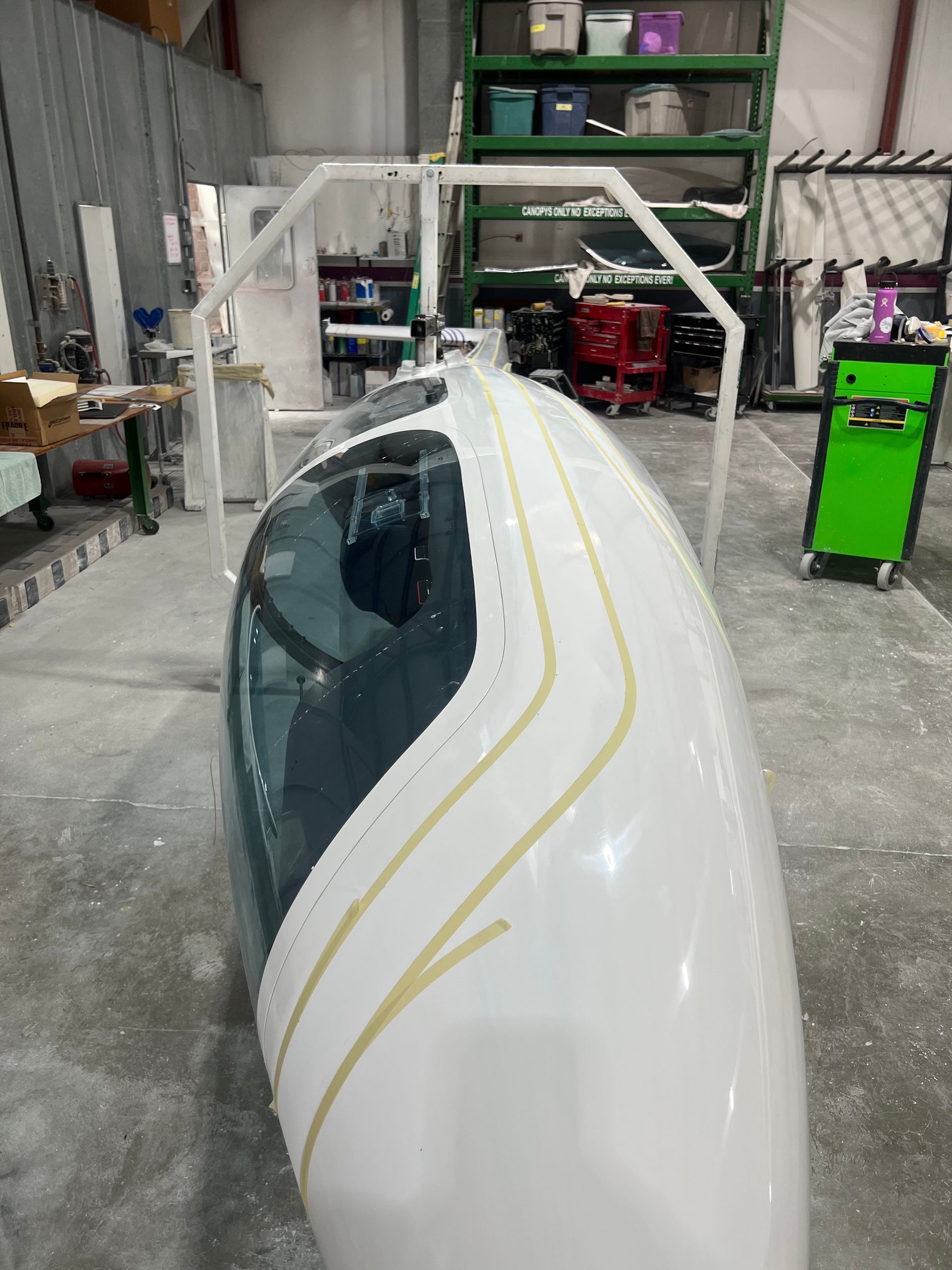A white boat is sitting in a garage with a green toolbox in the background.