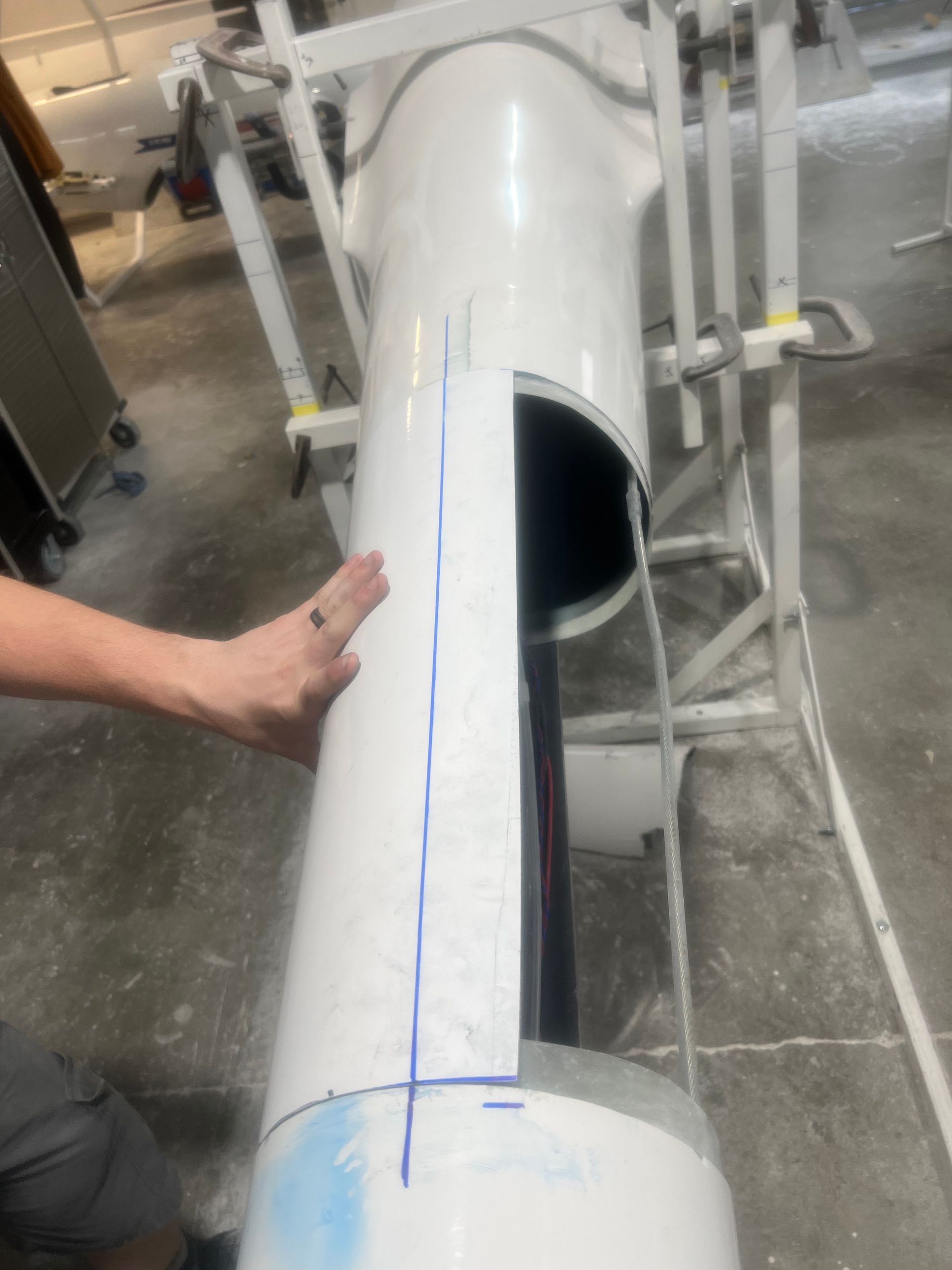 A person is measuring a white pipe with a blue line on it.