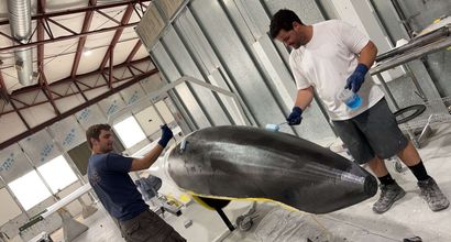 Two men are working on a large piece of metal in a factory.