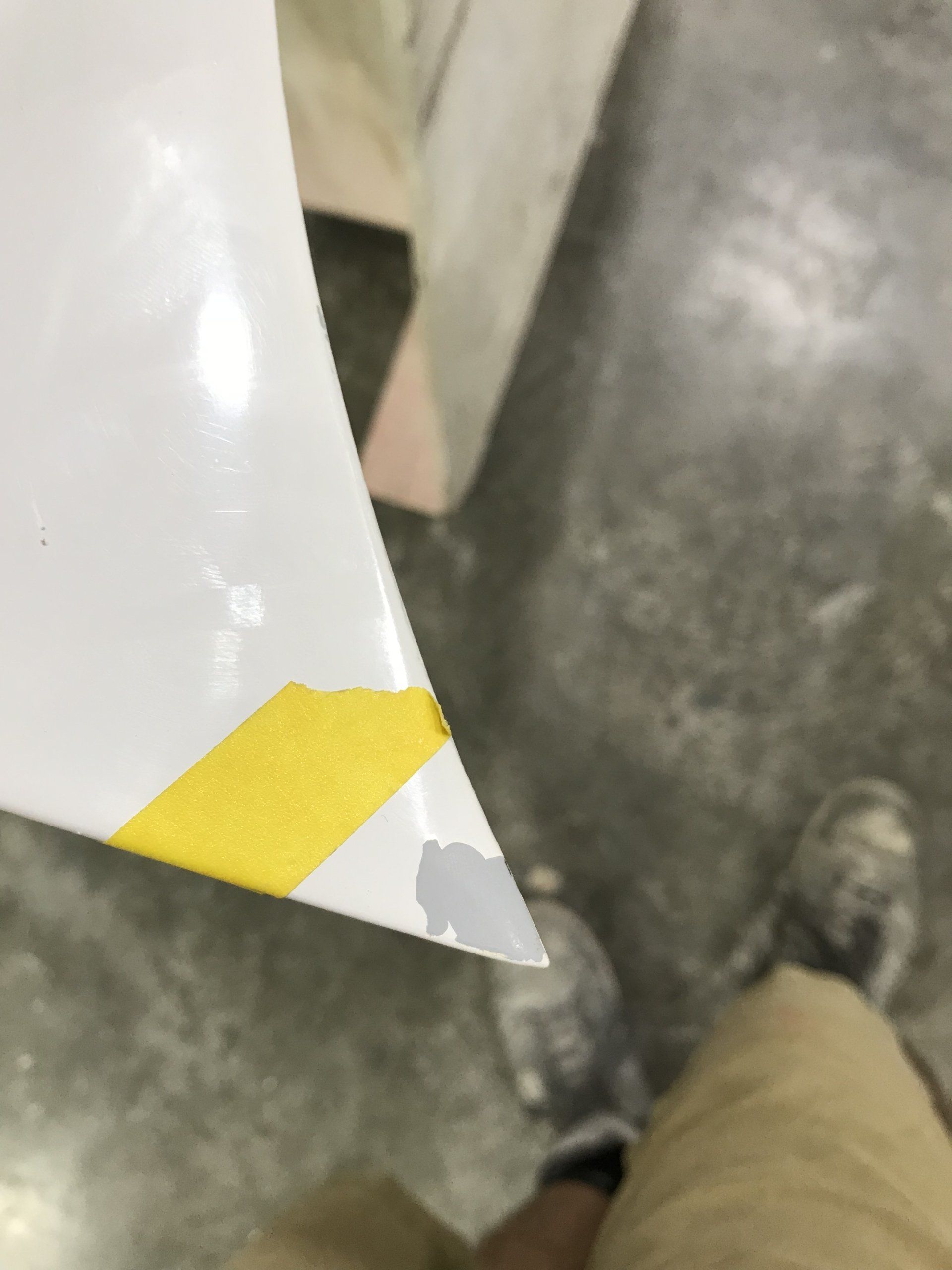 A person is standing next to a piece of paper with yellow tape on it.