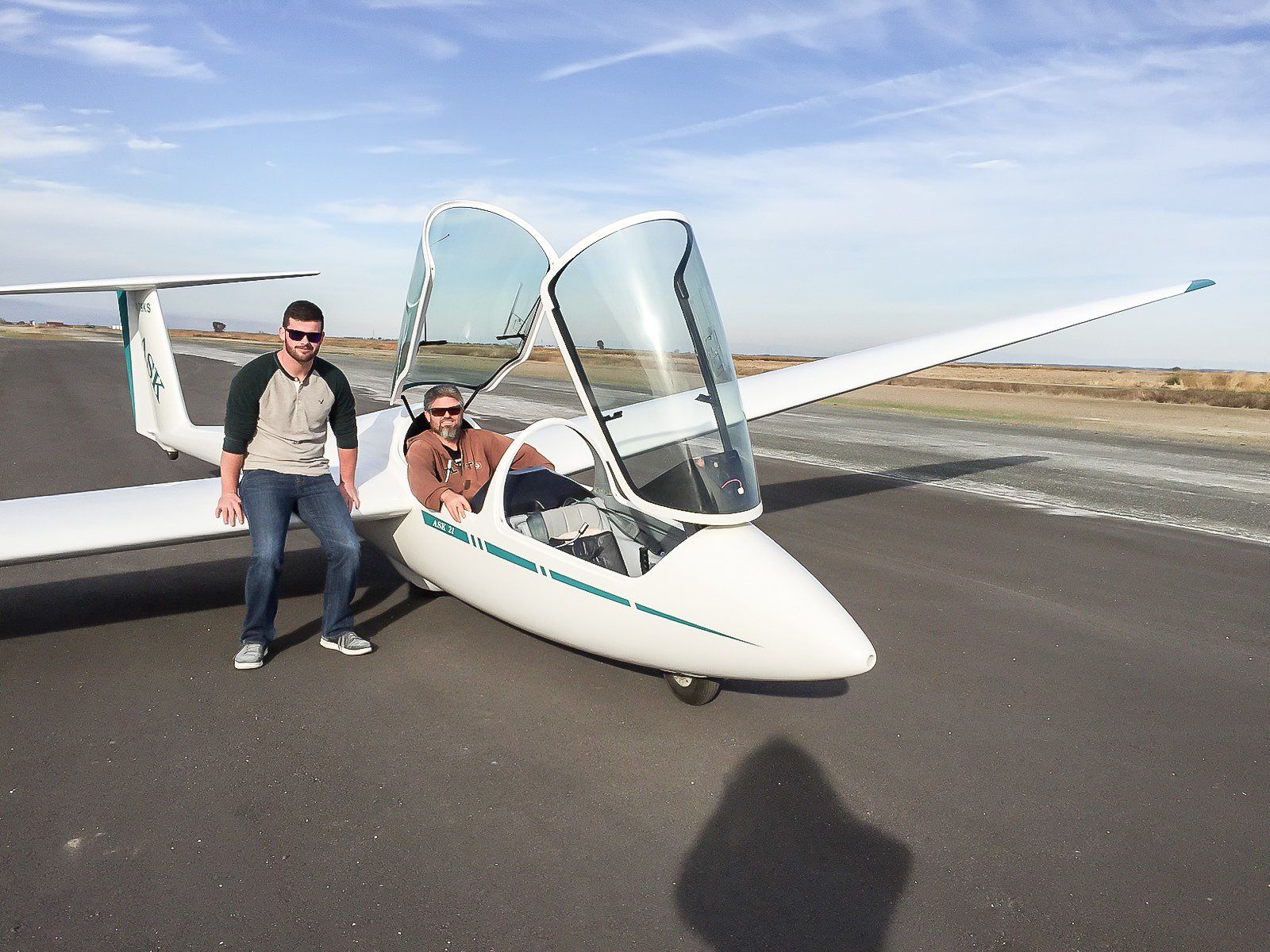 Two men are standing next to a small plane on a runway