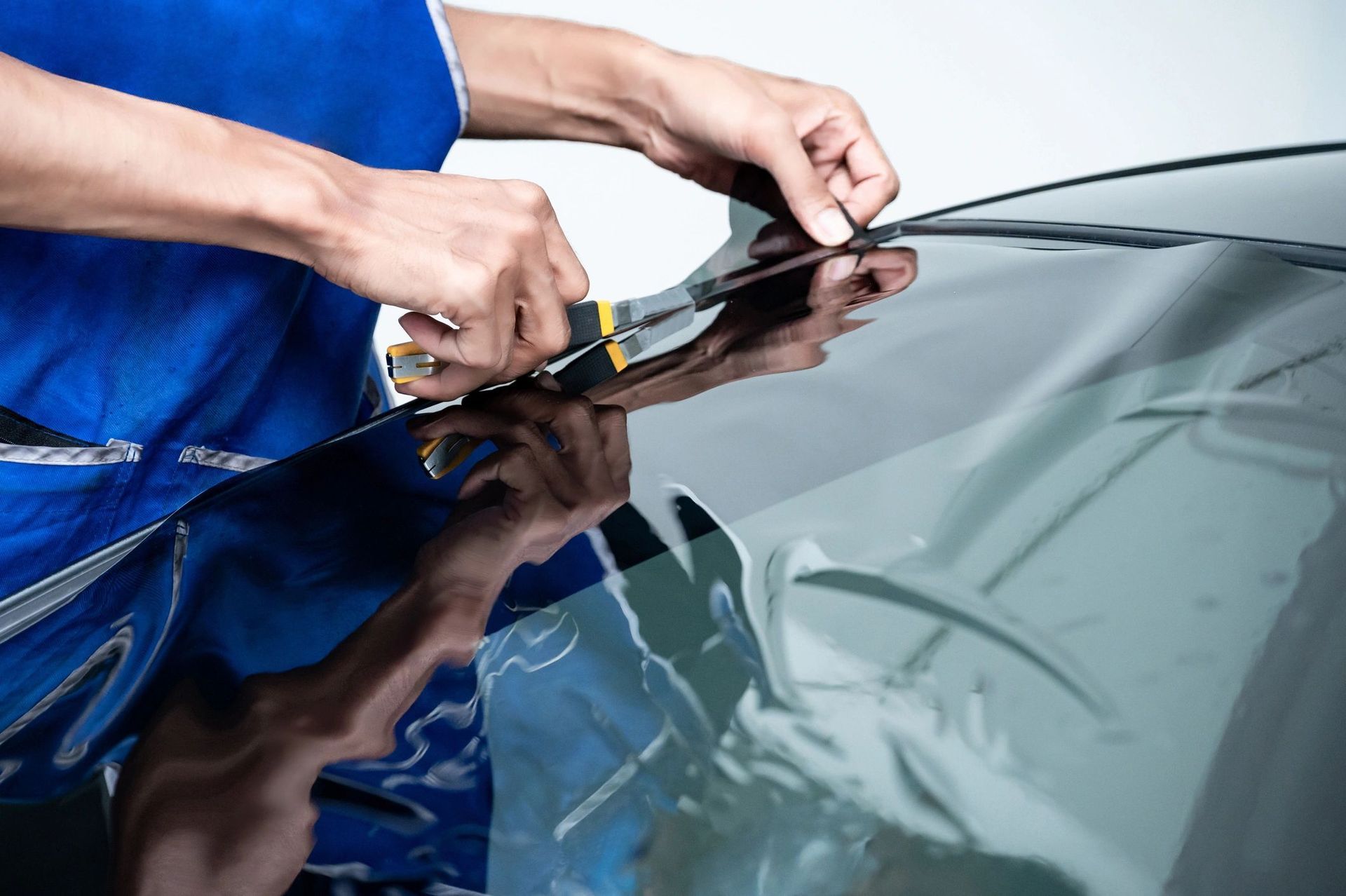 A man is cutting a piece of tinted glass on a car windshield.