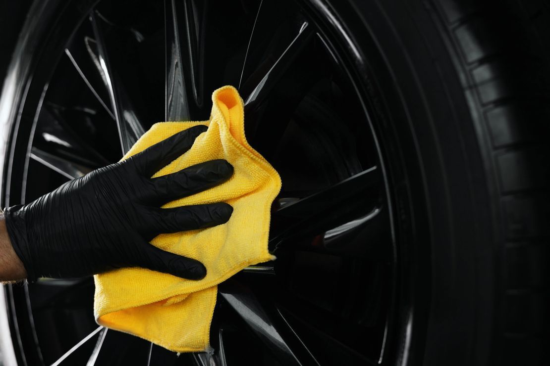 A person is cleaning a car wheel with a yellow cloth.