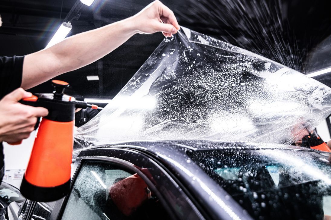 A person is applying a protective film to the windshield of a car.