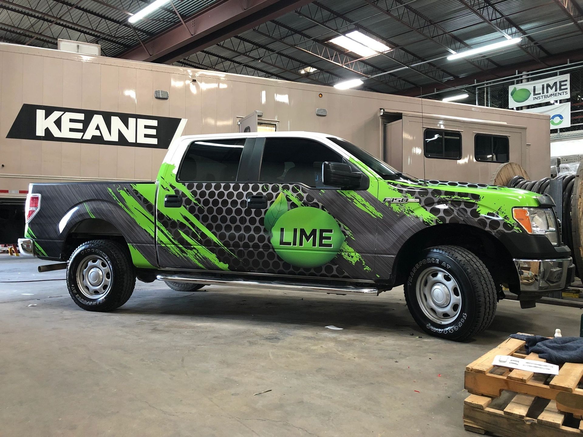 A green and black truck is parked in a garage next to a trailer.