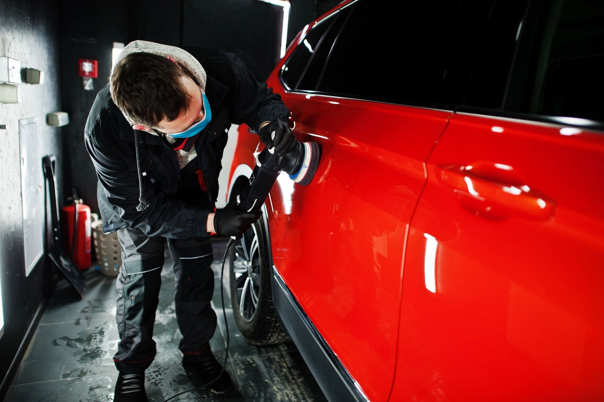 A man is polishing a red car in a garage.