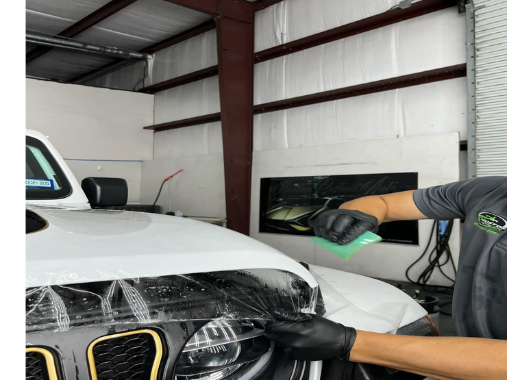 A man is covering the headlights of a white jeep with plastic wrap.