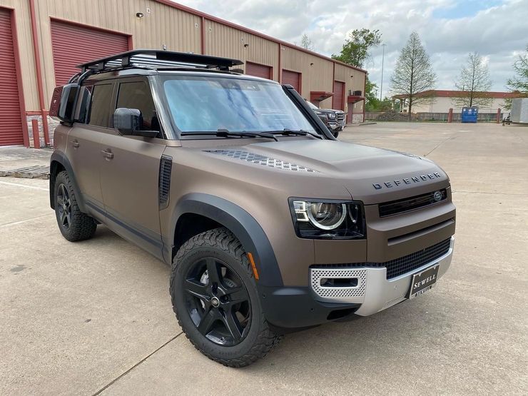 A brown land rover defender is parked in front of a building.